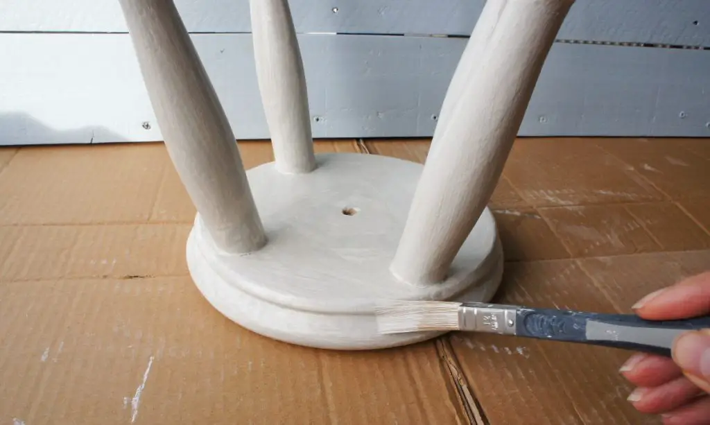 applying grey paint to wooden stool