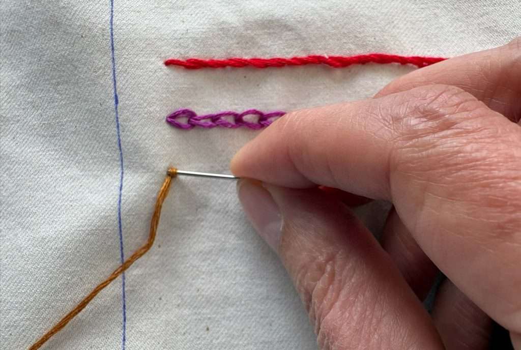 fench knot forming in mustard coloured yarn on a sampler