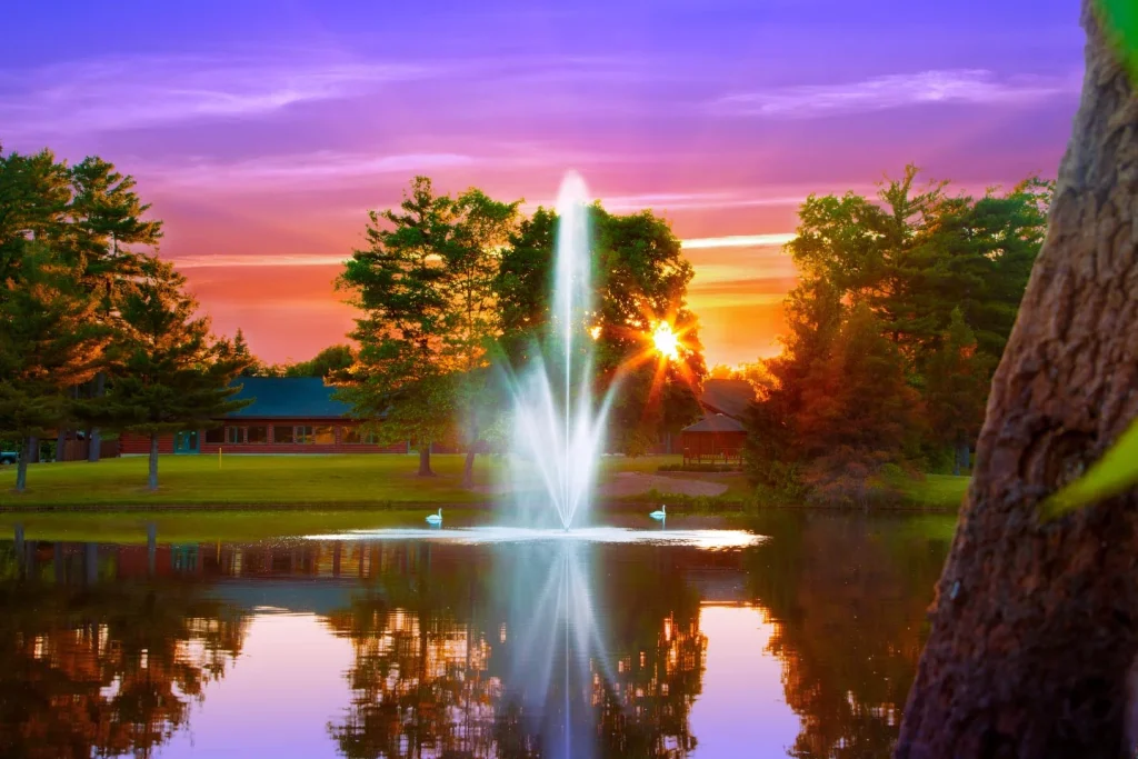 Vibrant sunset behind a pond fountain.
