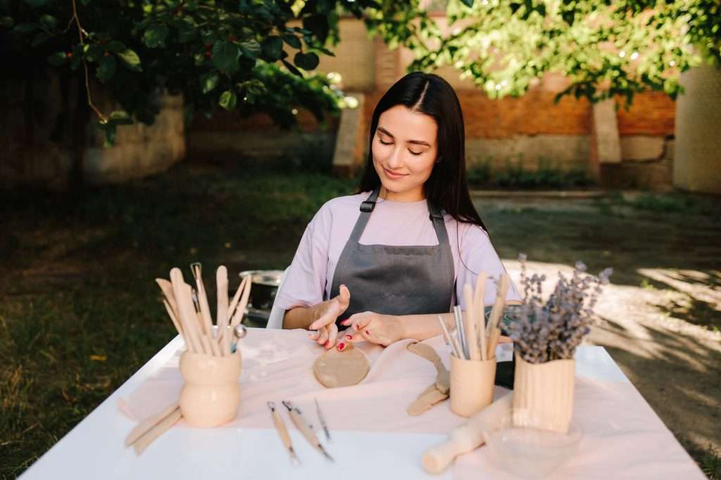 woman sitting outside at a table doing pottery